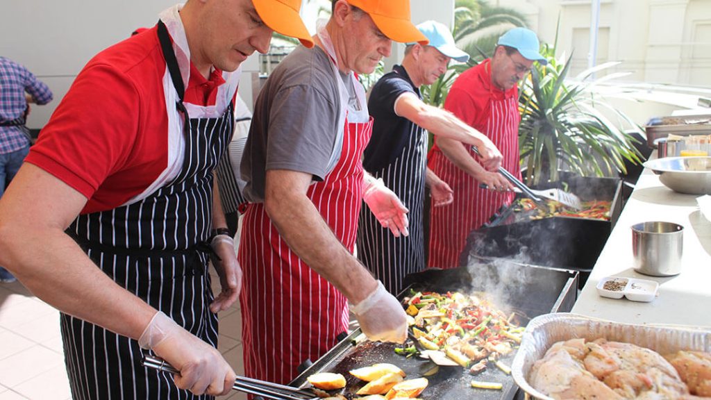Participants engaged in a MasterChef team building event in an outdoor garden setting.