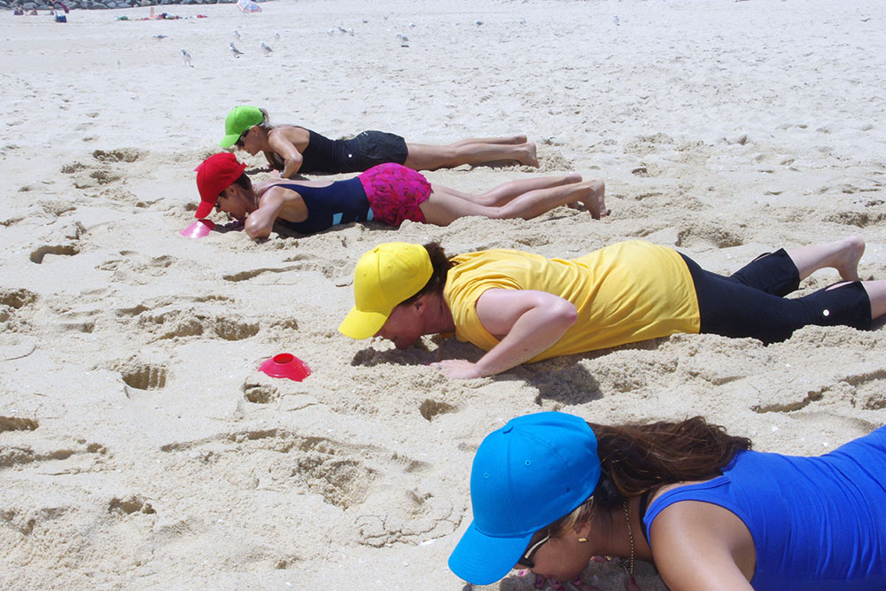 A group of colleagues participating in Beach Olympics team building activities on a sunny beach.